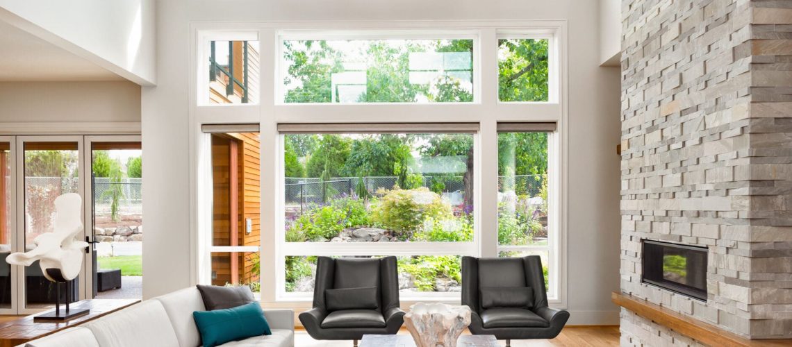 Beautiful living room interior with hardwood floors, huge bank of windows, tall vaulted ceiling, and fireplace in new luxury home